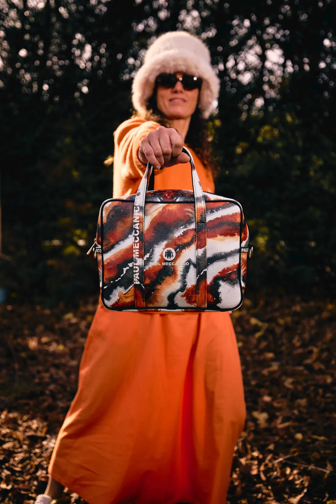 Una donna con abito arancione e cappello di pelliccia che tiene una borsa colorata Paul Meccanico
